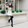 Fashionable brunette girl with long hair, dressed in a raincoat, high black boots with heels with a hand bag waiting for