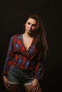 Fashionable young woman with long hair posing in checkered jacket on a dark studio background with shadows Royalty Free Stock Photo