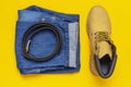 Fashionable concept. Men`s casual wear, yellow work boots from natural nubuck leather, blue jeans and brown belt on bright yellow Royalty Free Stock Photo