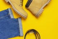 Fashionable concept. Men`s casual wear, yellow work boots from natural nubuck leather, blue jeans and brown belt on bright yellow Royalty Free Stock Photo