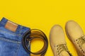 Fashionable concept. Men`s casual wear, yellow work boots from natural nubuck leather, blue jeans and brown belt on bright yellow Royalty Free Stock Photo