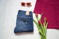 Fashionable concept. Tulips, blue jeans, part of burgundy top, sunglasses. Spring wardrobe. Wooden background