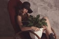 Fashionable confident woman with long legs in black dress and hat, sitting on rocking chair posing in studio with beton background Royalty Free Stock Photo