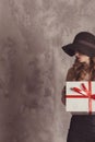 Fashionable confident woman with long legs in black dress and hat, sitting on rocking chair posing in studio with beton background Royalty Free Stock Photo