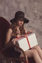 Fashionable confident woman with long legs in black dress and hat, sitting on rocking chair posing in studio with beton background Royalty Free Stock Photo