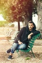 Fashionable cool young man relaxing on a bench in a park with trees Royalty Free Stock Photo