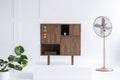 Fashionable dark wooden commode in bright interior with green plant and copper fan