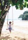 Fashionable dressed Woman sits on tree swing on the wide sandy o