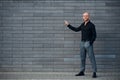 Fashionable elegant man standing outdoors against grey wall and shows to the left by finger Royalty Free Stock Photo