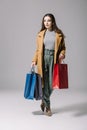 fashionable elegant woman in beige coat holding shopping bags on grey. Royalty Free Stock Photo