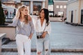 Fashionable european ladies talking while walking around city. Amazing brunette woman with camera looking at her friend Royalty Free Stock Photo