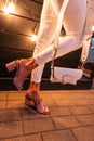 Fashionable female legs in vintage jeans in leather summer shoes with heels with a white handbag near a wooden wall with bright Royalty Free Stock Photo