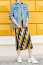 Fashionable female look with a denim blue jacket, a skirt with diagonal lines and white sneakers. Street fashion.