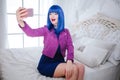 Fashionable freak. Glamour happy beautiful woman with blue hair and trendy makeup is holding computer and doing selfie