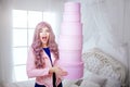 Fashionable freak. Glamour happy beautiful woman with long lilac hair is holding pink boxes while standing in white