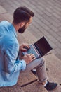 A fashionable freelancer male with a full beard and haircut, wearing casual clothes, working on a laptop computer