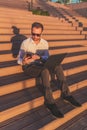 Fashionable freelancer using smartphone and laptop while sitting on stairs during sunset Royalty Free Stock Photo