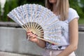 Fashionable girl with hands fan on a hot sunny summer day sitting on a park bench