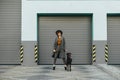 Fashionable girl in a hat and with curly hair holds a leash with a dog in her hand and poses at the camera against a gray wall