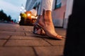 Fashionable girl in stylish beige summer shoes stands on a tile in the city in the evening, close up