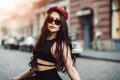 Fashionable girl wearing sunglasses and hat walking on city street looking at camera Royalty Free Stock Photo