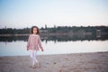 The fashionable girl in white trousers near the lake. The child costs barefoot on sand