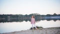 The fashionable girl in white trousers near the lake. The child costs barefoot on sand