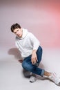 Fashionable handsome young European male model dressed in white sweatshirt, blue jeans and white sneakers posing in Royalty Free Stock Photo