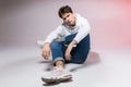 Fashionable handsome young European male model dressed in white sweatshirt, blue jeans and white sneakers posing in studio on a Royalty Free Stock Photo