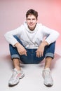 Fashionable handsome young European male model dressed in white sweatshirt, blue jeans and white sneakers posing in studio on a Royalty Free Stock Photo