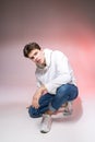 Fashionable handsome young European male model dressed in white sweatshirt, blue jeans and white sneakers posing in studio on a Royalty Free Stock Photo