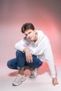 Fashionable handsome young European male model dressed in white sweatshirt, blue jeans and white sneakers posing in studio on a Royalty Free Stock Photo