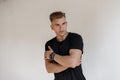 Fashionable handsome young man with hairstyle in a black t-shirt with a watch poses near a white wall on the street Royalty Free Stock Photo