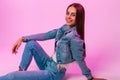 Fashionable happy young woman with lovely smile in stylish youth blue jeans clothes sits and beautiful smiling near vintage pink Royalty Free Stock Photo