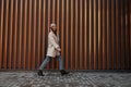 Fashionable joyful young woman with a beautiful smile steps near a metal vintage wall in the city. Funny cute girl model in trendy