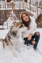 Fashionable joyful young woman having fun with lovely husky dog in snow on the street. True emotions, happy moments in