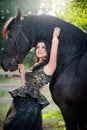 Fashionable lady with black royal dress near brown horse. Beautiful young woman in luxurious elegant dress posing with a horse Royalty Free Stock Photo