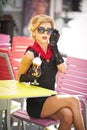 Fashionable lady with little black dress and red scarf sitting on chair in restaurant, outdoor shot in sunny day. Young blonde Royalty Free Stock Photo