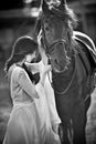 Fashionable lady with white bridal dress near brown horse. Beautiful young woman in a long dress posing with a friendly horse Royalty Free Stock Photo