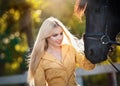 Fashionable lady with yellow coat near black horse in forest.