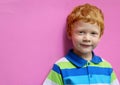 Fashionable little boy. Red-haired handsome kid model wearing trendy striped casual shirt posing against pink wall