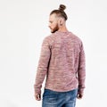 Fashionable man with beard and bun hairstyle dressed in pock-marked long sleeve sweater and jeans poses in the studio on