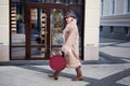 Fashionable mature woman walking in the city, dressed in a long beige coat, Cossack boots, hat with animal print and