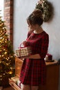 Fashionable model girl with trendy hairstyle in plaid red dress holding the present box near the Christmas tree. Young Royalty Free Stock Photo