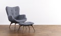 Fashionable modern gray armchair with wooden legs, ottoman against a white wall in the interior. Furniture, interior object,