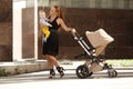 Fashionable modern mother on a city street with a pram. Young mo Royalty Free Stock Photo