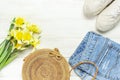 Fashionable natural organic round rattan bag, denim shorts, beige women`s espadrilles, yellow narcissus daffodil flowers on light