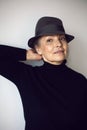 fashionable older woman in black clothes and a hat stands against a white wall Royalty Free Stock Photo