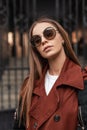 Fashionable portrait beautiful young hipster woman in trendy trench coat in stylish dark sunglasses with long hair near vintage Royalty Free Stock Photo