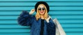 Fashionable portrait stylish blonde smiling woman with shopping bags wearing a blue faux fur coat, black round hat on colorful